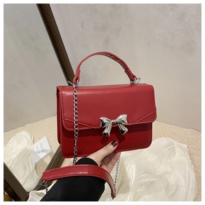 Detail of red crossbody bag featuring silver metal bow and polished chain strap
