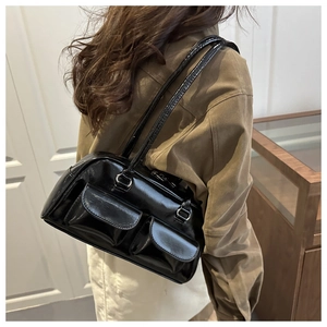 Detail view of glossy black faux leather shoulder bag with two front pockets on a model