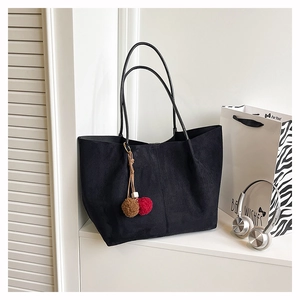 Detail of black suede tote bag with plush ball charm and long leather straps