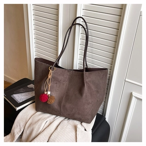 Detail of dark brown suede tote bag featuring a tassel charm and slim shoulder straps