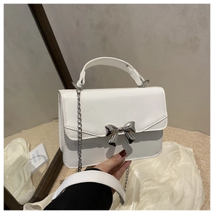 Close-up of white crossbody bag with silver bow ornament and metallic chain strap