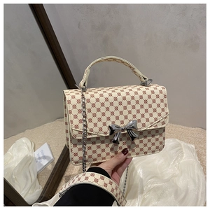 Detail of cream crossbody bag with vintage monogram patterns and metal bow clasp