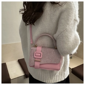 Close-up of pink sequined handbag with decorative buckle worn by a model in a white sweater