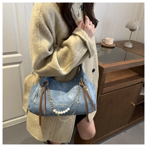 Close-up of blue denim tote bag with gold chain, white pearls and brown leather pullers
