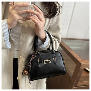 Detail view of black shell bag featuring golden horsebit buckle and woven pendant