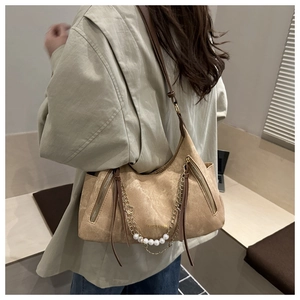 Close-up of brown suede shoulder bag featuring decorative gold chains and pearl accents
