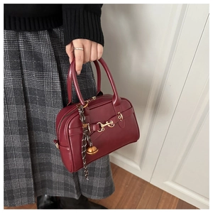 Detail of burgundy Boston handbag featuring gold horsebit accent and sleek leather finish