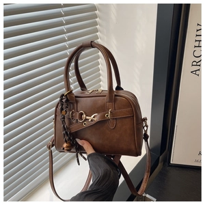 Detailed view of brown leather Boston bag featuring decorative metal buckle and woven charm