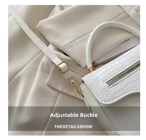Détail de la boucle dorée réglable et du crochet métallique sur un sac blanc croco
