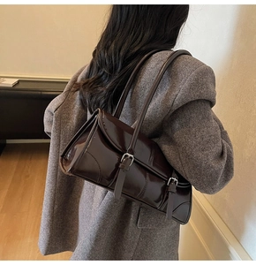 Close-up of a vintage dark brown patent leather shoulder bag on a grey wool coat