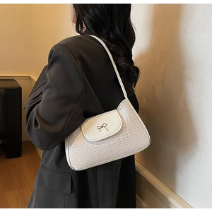 Detail of white faux crocodile leather underarm bag featuring a small metal bow clasp