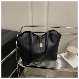 Detail of black lychee texture leather tote bag with gold metal clasp on a metal rack