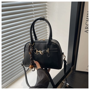 Detail of black shell crossbody bag with golden hardware and braided pendant accessory