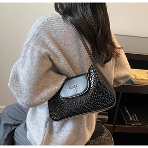Detail of black crocodile texture shoulder bag featuring a silver metal bow buckle clasp