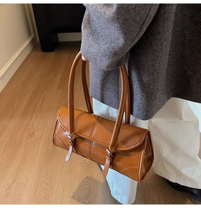 Detail view of brown leather baguette bag with belt buckles on charcoal blazer