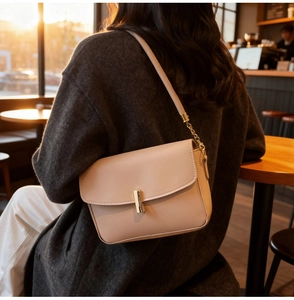 Detail of a beige leather shoulder bag featuring a golden cylindrical clasp and chain strap