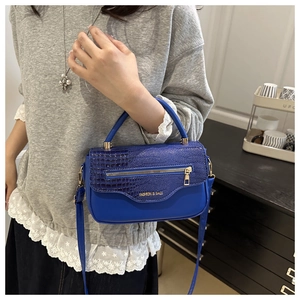Détail du rabat bleu à texture crocodile et fermeture éclair dorée sur le sac bandoulière