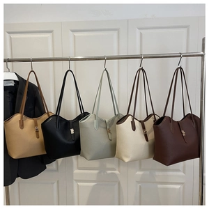 Detail view of five colors of leather tote bags with metal buckles on a garment rack