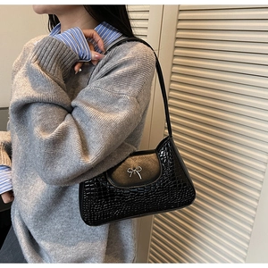 Detail of black faux crocodile leather underarm bag with silver bow buckle on model