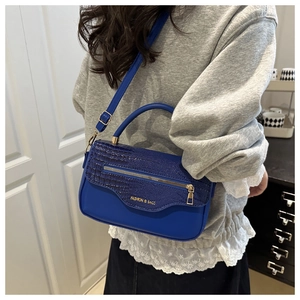 Détail du sac à main bleu motif crocodile avec zip métallique et texte mode porté épaule