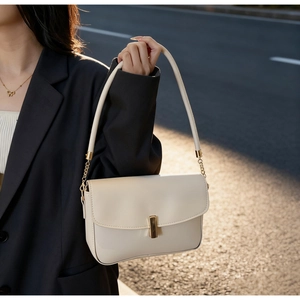 Detail of a creamy white minimalist handbag with gold metal lock and leather chain strap