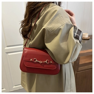 Detail of red leather shoulder bag with gold horsebit buckle on khaki trench coat