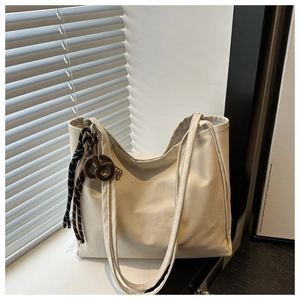 Detail of cream faux leather tote bag featuring a decorative woven knot charm and twin straps