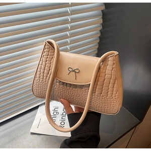 Detail of beige shoulder bag featuring croc-embossed texture and metal bow closure