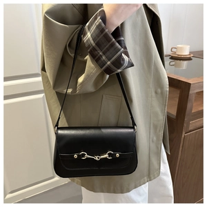 Detail of minimalist black leather crossbody bag featuring a golden horsebit metal buckle