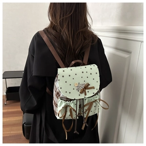 Detail of mint green backpack with star pattern, brown bow, and plaid side pocket panels