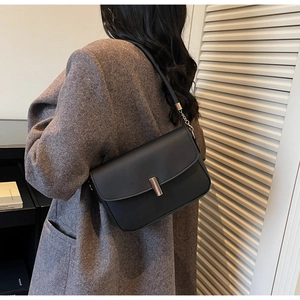Side view of a minimalist black leather square bag worn by a model in a modern room