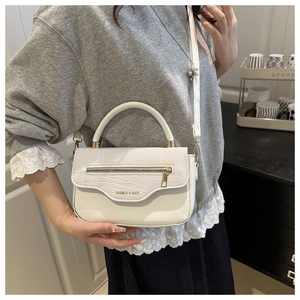 Gros plan d'un sac à bandoulière blanc à motif crocodile porté par un mannequin chic