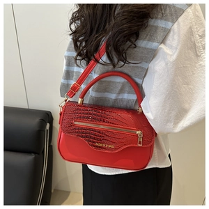 Détail du sac à main rouge motif crocodile avec zip doré porté par un mannequin en tenue