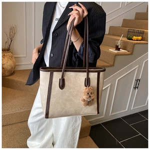 Detail shot of vintage off-white leather tote bag with brown trim and plush bear charm
