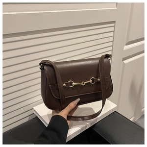 Detailed close-up of dark brown handbag with golden horsebit buckle and long shoulder strap