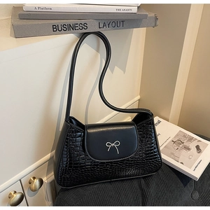 Detail of black faux crocodile leather shoulder bag with silver bow accent