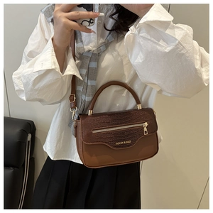 Détail du rabat motif crocodile et du zip doré sur un sac bandoulière marron