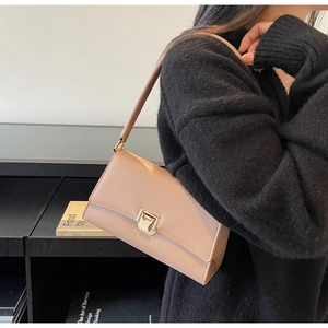 Close-up of beige leather shoulder bag with gold square buckle worn by a model