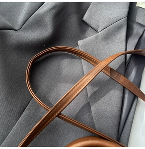 Dettaglio della tracolla in pelle marrone con cuciture precise su un blazer grigio