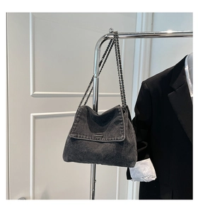 Detail of grey denim messenger bag with silver metal chain strap and logo plate