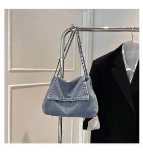 Detail of washed denim shoulder bag featuring dual chain straps and flap closure design