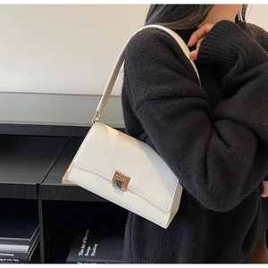 Detail of white leather shoulder bag with gold twist lock on black knit outfit
