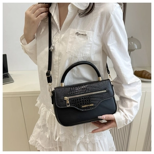 Détail du sac noir à texture crocodile avec zip doré porté par un mannequin en blanc