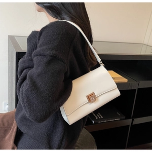 Close-up of minimalist white leather shoulder bag with a gold metallic twist lock