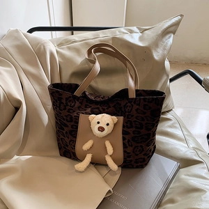 Large leopard print tote bag with 3D teddy bear charm on a stylish beige chair