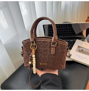 Dettaglio borsa leopardata con ciondolo in legno e logo dorato su trama opaca fine