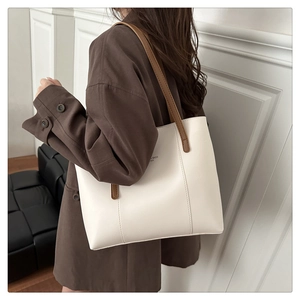 Detail of a minimalist white tote bag with brown straps styled with a brown blazer