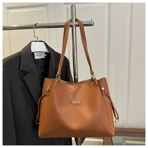 Detail of caramel tote bag showing the side drawstring, silver metal ring, and faux leather texture