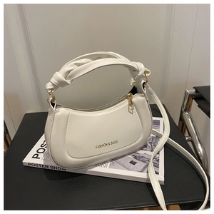 Detail view of white crossbody bag with knot handle and gold hardware on leather chair