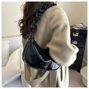 Detail of black patent leather crescent bag with ruched strap and minimalist typography